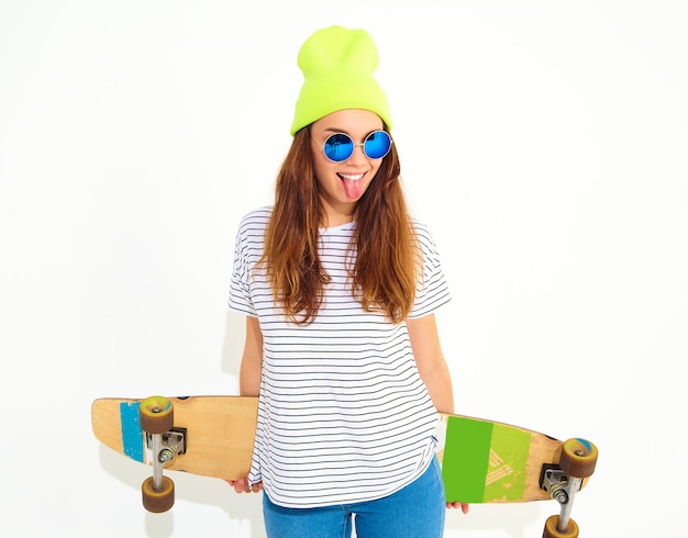 Retrato de mujer joven elegante modelo en ropa casual de verano en gorro amarillo posando con escritorio de longboard. Aislado en blanco