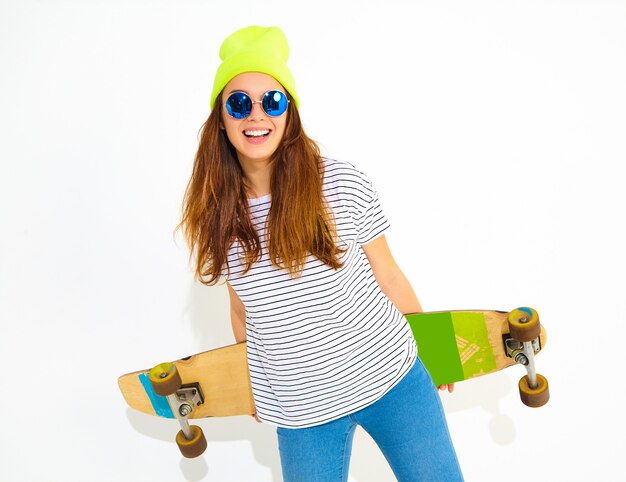 Retrato de mujer joven elegante modelo en ropa casual de verano en gorro amarillo posando con escritorio de longboard. Aislado en blanco