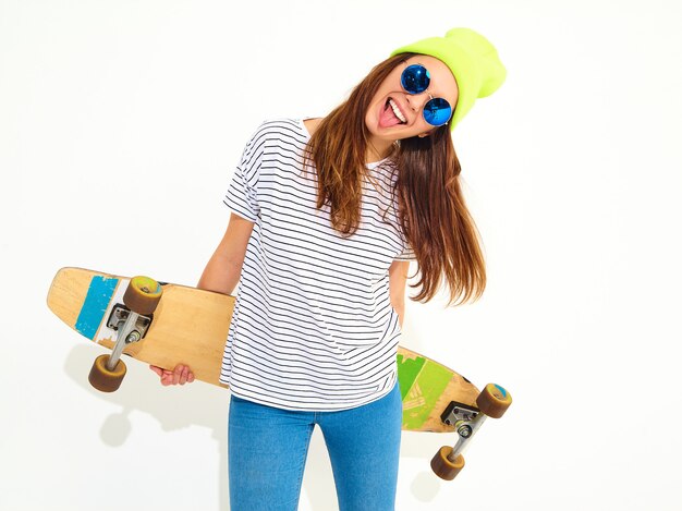 Retrato de mujer joven elegante modelo en ropa casual de verano en gorro amarillo posando con escritorio de longboard. Aislado en blanco