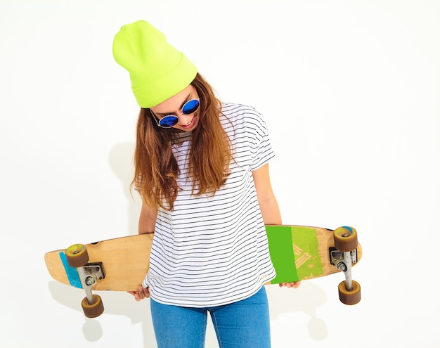 Retrato de mujer joven elegante modelo en ropa casual de verano en gorro amarillo posando con escritorio de longboard. Aislado en blanco