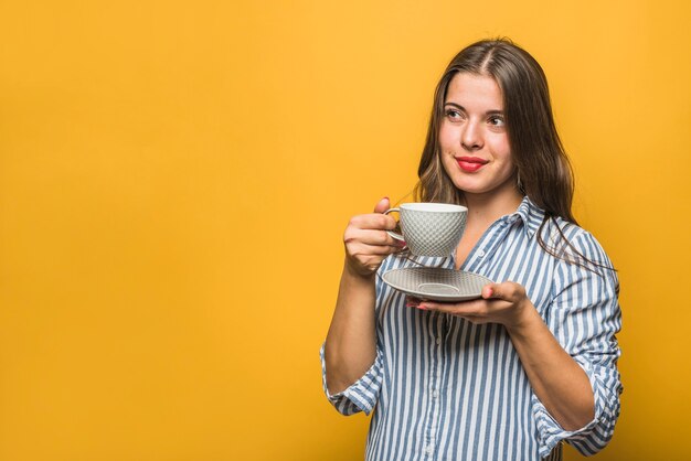 Retrato de una mujer joven elegante que sostiene la taza en las manos que miran lejos