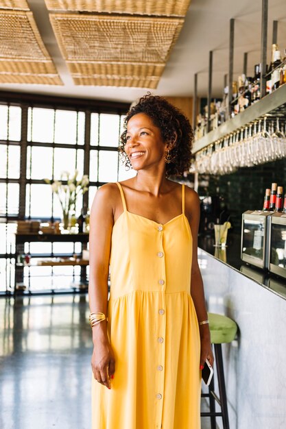 Retrato de la mujer joven elegante sonriente que se coloca en el restaurante