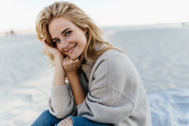 Retrato de mujer joven encantadora con pelo ciego, vestida con suéter de cachemira. mujer sentada en la playa y disfruta del día de primavera.