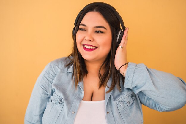 Retrato de mujer joven escuchando música con auriculares al aire libre contra la pared amarilla