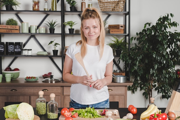 Retrato de mujer joven con espátula de madera en la cocina