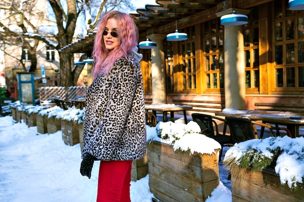 Retrato de mujer joven con estilo posando en la calle con cabello rosado inusual, chaqueta de leopardo de moda y gafas vintage