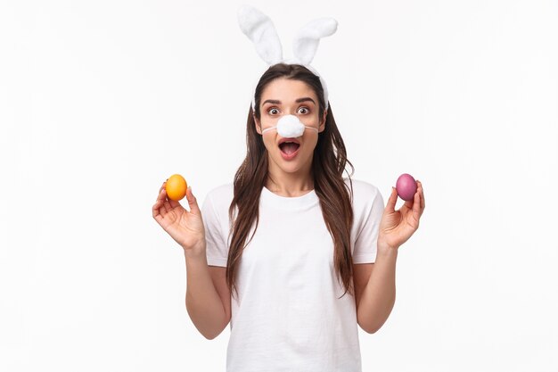 Retrato de mujer joven expresiva usa orejas de conejo y nariz, sosteniendo huevos coloreados