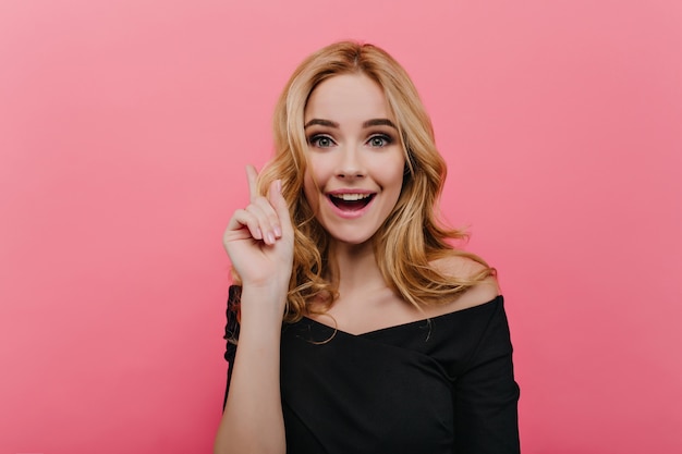 Retrato de mujer joven extática con expresión de la cara feliz riendo en la pared de color rosa brillante. Foto de interior de la encantadora modelo femenina viste un elegante atuendo negro.