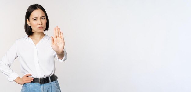 Retrato de mujer joven extendiendo una mano parada tabú signo rechazando declinando algo de pie sobre fondo blanco.