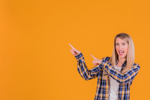 Retrato de una mujer joven feliz apuntando sus dedos contra un fondo naranja