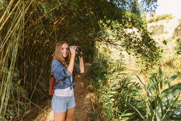 Retrato de una mujer joven feliz con binoculares de pie en el bosque