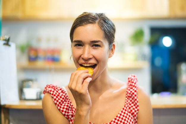 Retrato de mujer joven feliz comiendo galletas en la cocina