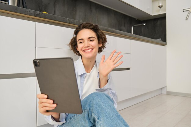 Retrato de mujer joven feliz se conecta a ondas de video chat en tableta digital y sonriente se sienta en hom