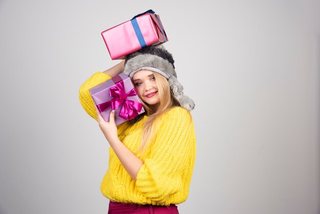 Retrato de mujer joven feliz con gorra trayendo un montón de regalos.