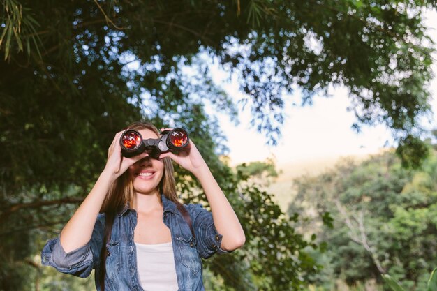 Retrato de una mujer joven feliz mirando a través de binoculares en el bosque
