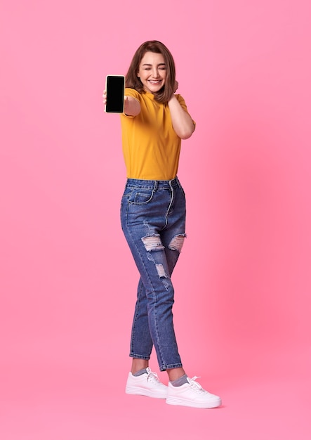 Foto gratuita retrato de mujer joven feliz mostrando en teléfono móvil con pantalla en blanco sobre rosa.