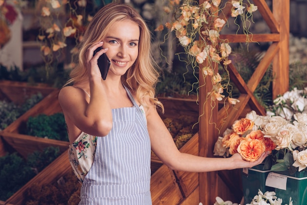 Foto gratuita retrato de una mujer joven feliz que habla en el teléfono móvil que sostiene la flor disponible