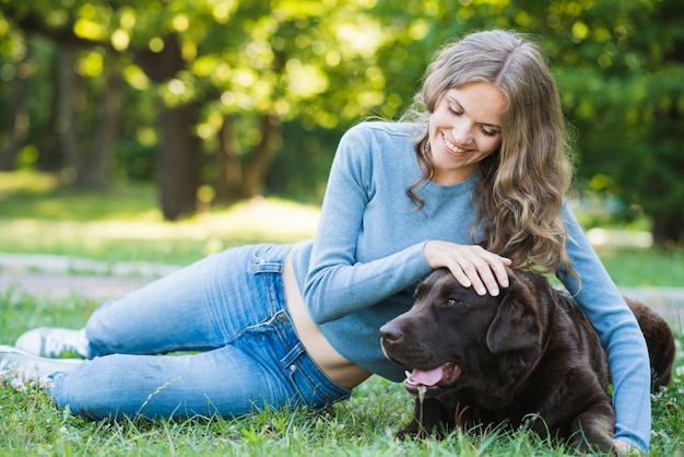 Retrato de una mujer joven feliz que se inclina en perro sobre hierba verde