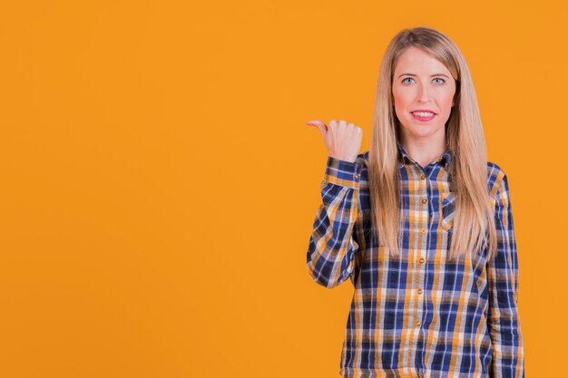 Retrato de una mujer joven feliz que muestra gesto del pulgar contra un fondo anaranjado