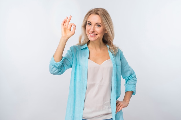 Foto gratuita retrato de una mujer joven feliz que muestra la muestra aceptable contra el contexto blanco