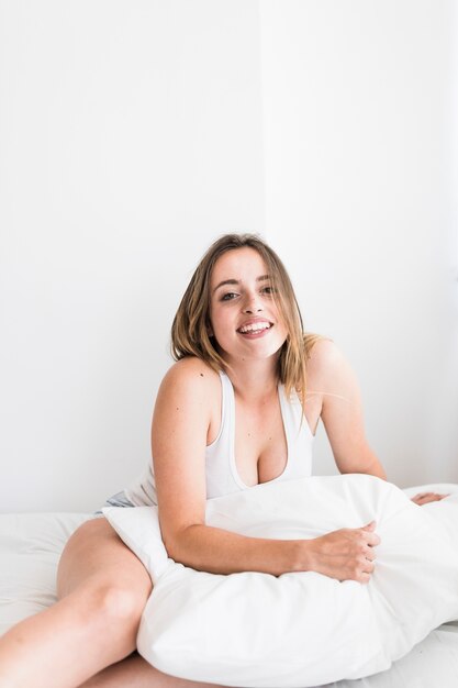 Retrato de una mujer joven feliz que se sienta en cama