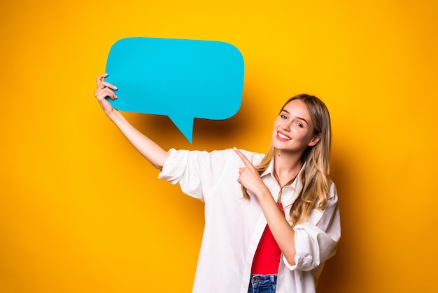 Retrato de una mujer joven feliz que sostiene la burbuja del discurso vacía que se encuentran aisladas sobre la pared amarilla