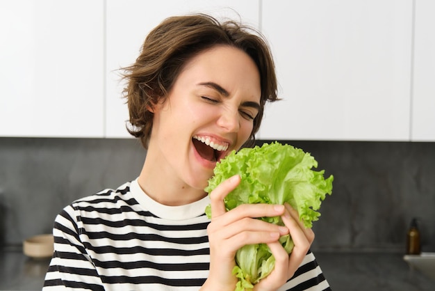 Foto gratuita retrato de una mujer joven feliz y saludable siguiendo su dieta posando con hoja de lechuga y sonriendo