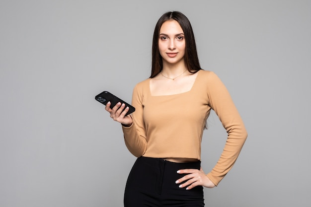 Retrato de una mujer joven feliz con smartphone aislado en una pared gris