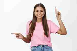 Foto gratuita retrato de mujer joven feliz sonriendo, señalando con el dedo dos lados, mostrando direcciones izquierda y arriba, de pie contra el fondo blanco.