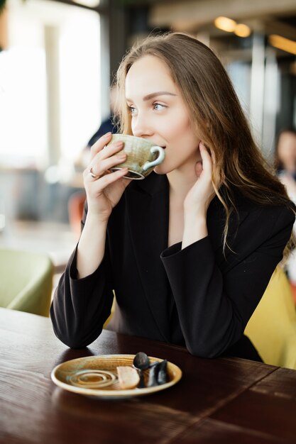 Retrato de mujer joven feliz con taza en manos bebiendo café por la mañana en el restaurante