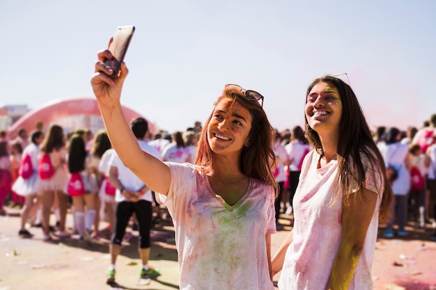 Retrato de una mujer joven feliz tomando selfie en el teléfono móvil durante el festival holi
