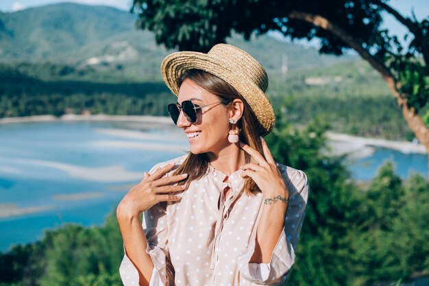 Retrato de mujer joven feliz en vestido de verano, gafas de sol y sombrero de paja