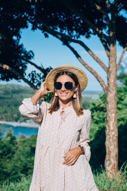 Retrato de mujer joven feliz en vestido de verano, gafas de sol y sombrero de paja