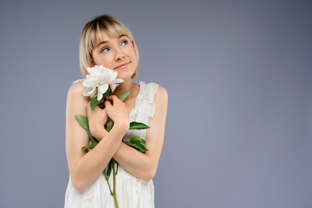 Retrato de mujer joven con flor sobre pared gris