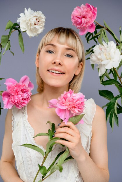 Retrato de mujer joven entre flores sobre pared gris
