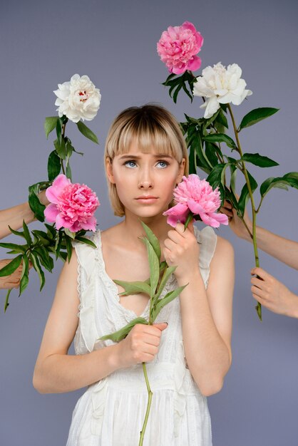 Retrato de mujer joven entre flores sobre pared gris