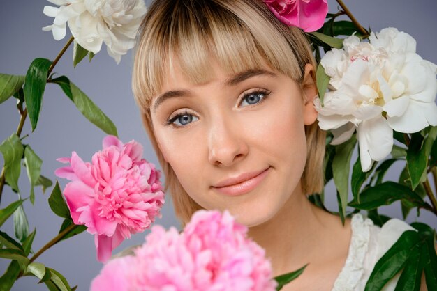 Retrato de mujer joven entre flores sobre pared gris