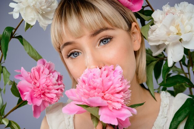 Retrato de mujer joven entre flores sobre pared gris