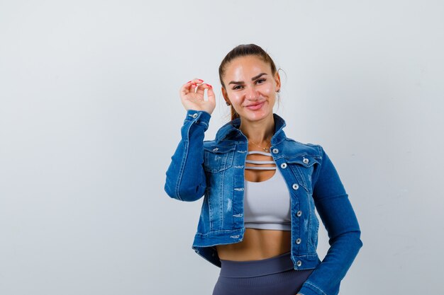 Retrato de mujer joven en forma mostrando garras imitando a gato en la parte superior, chaqueta de mezclilla y mirando alegre vista frontal