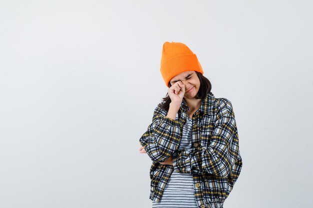 Retrato de mujer joven frotándose los ojos con sombrero naranja y camisa a cuadros