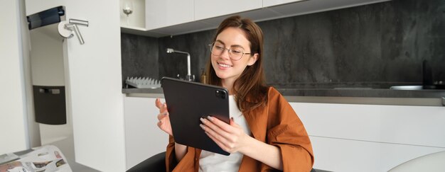 Retrato de una mujer joven con gafas mirando una tableta digital que trabaja desde casa y se conecta a una computadora remota