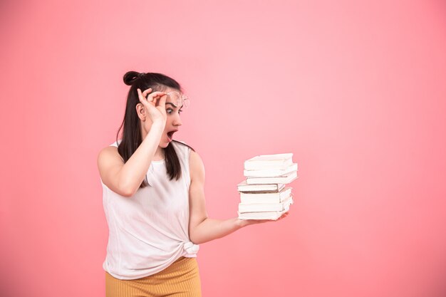 Retrato de una mujer joven con gafas sobre un fondo rosa con libros en sus manos.