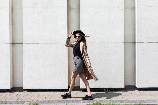 Retrato de una mujer joven con gafas de sol y sombrero negro caminando por la calle.