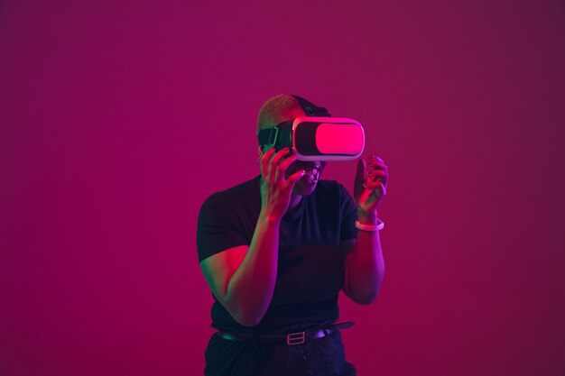 Retrato de mujer joven con gafas VR en pared rosa púrpura con luces de neón