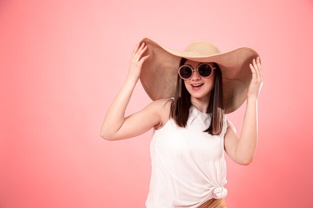 Retrato de una mujer joven con un gran sombrero de verano y gafas, sobre un fondo rosa. El concepto de verano.