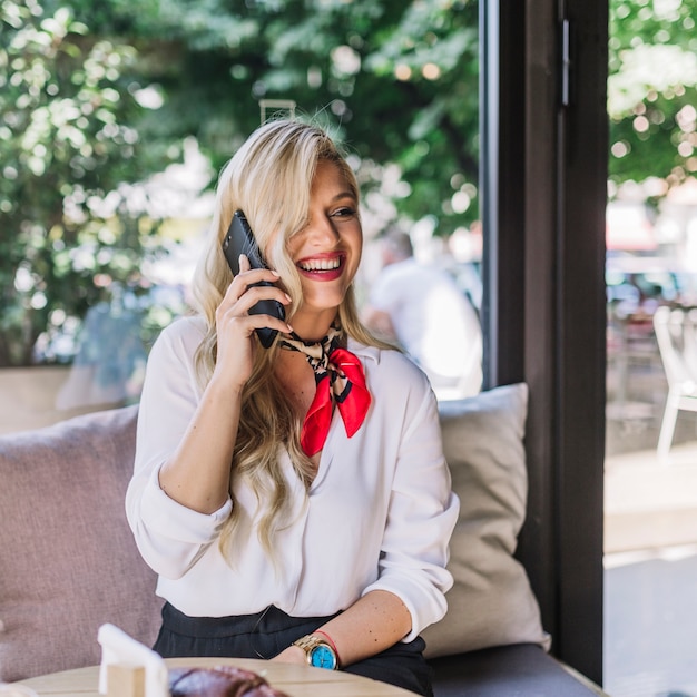 Foto gratuita retrato de una mujer joven hablando por teléfono inteligente en la cafetería.