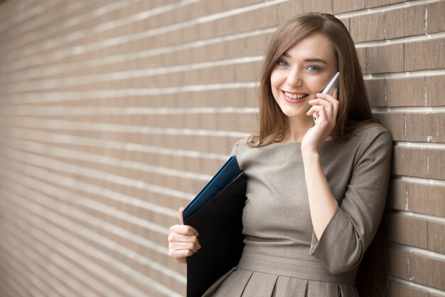 Retrato de mujer joven hablando por teléfono y mirando la cámara en la calle