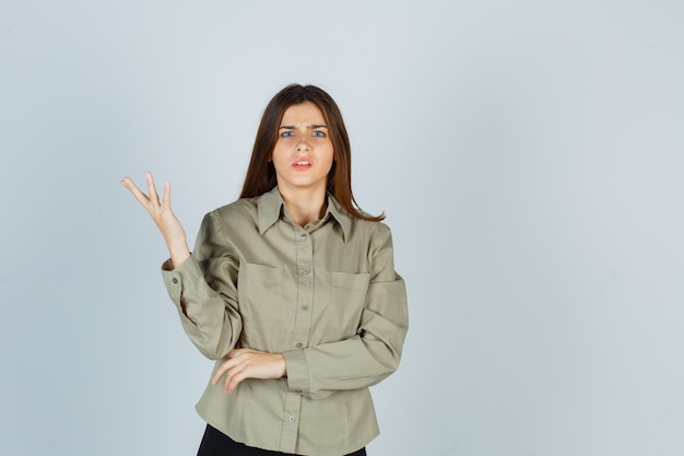 Retrato de mujer joven haciendo gesto de pregunta en camisa, falda y mirando perplejo vista frontal