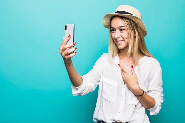 Retrato de mujer joven haciendo videollamadas en el teléfono inteligente, saludando a la cámara aislada sobre la pared azul