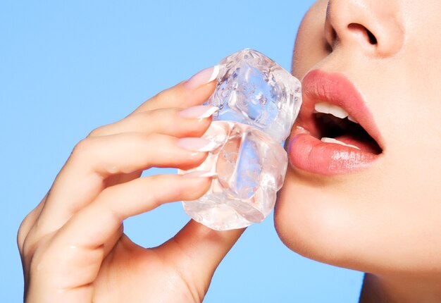 Retrato de mujer joven hermosa aplica el hielo a la cara en azul.